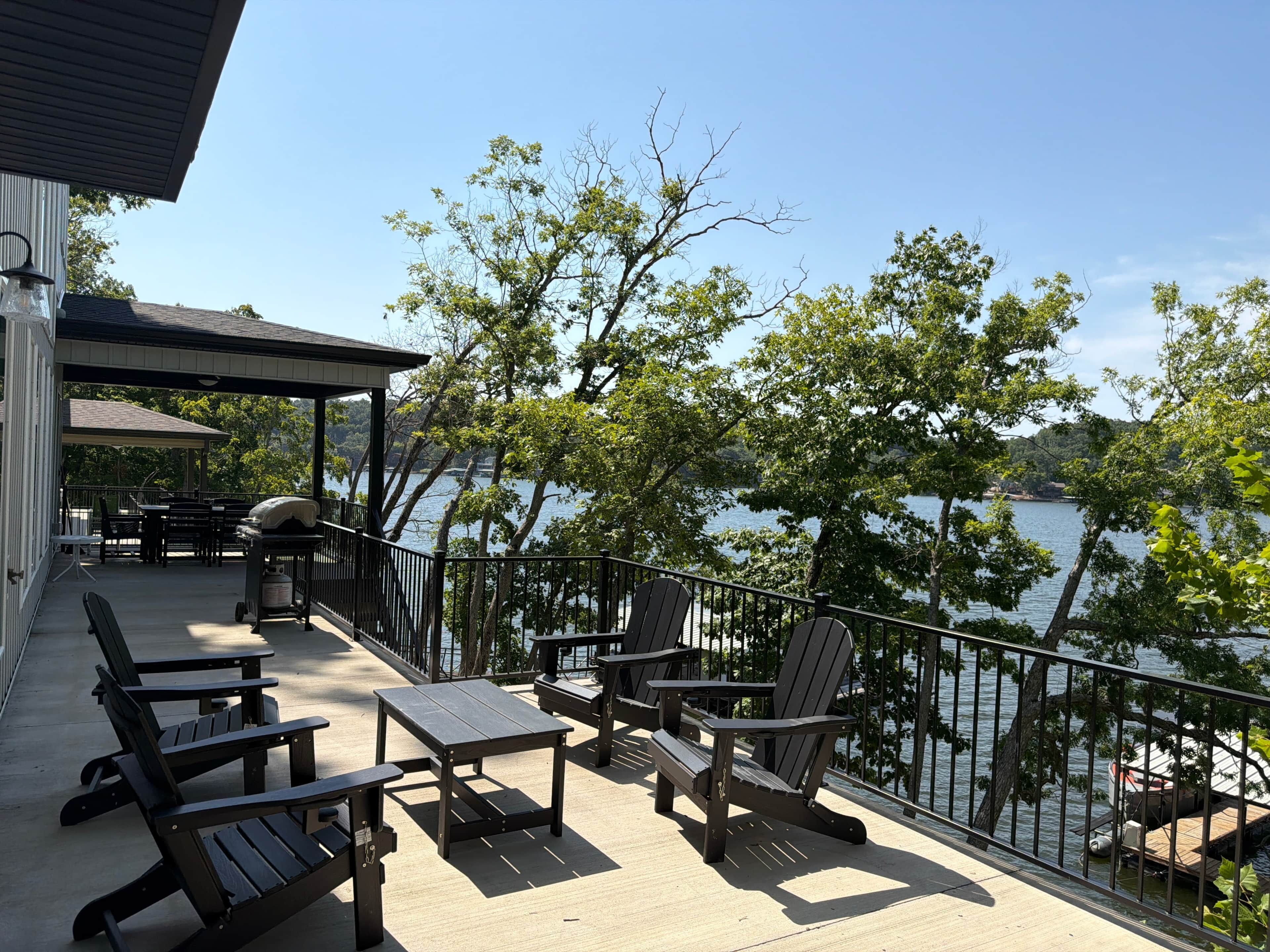 An outdoor deck with Adirondack chairs and tables, overlooking a body of water.