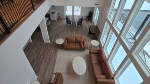 A spacious living area with a high ceiling, large windows, and a wooden floor.