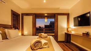 Ein Hotelzimmer mit einem großen Bett, zwei zusammengerollten Handtüchern, einem Fernseher und Blick auf die Stadt bei Dämmerung.