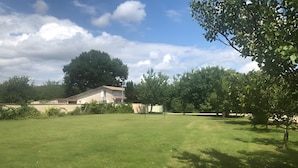 A grassy yard with a house, trees, and a clear sky.