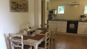 A dining area with a table and chairs, a kitchen with a microwave and oven, and a painting on the wall.
