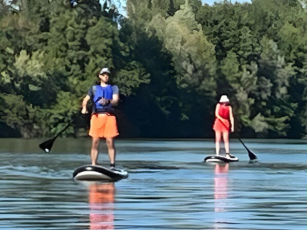 Deux personnes pratiquent le paddle sur un lac paisible, avec une forêt dense en arrière-plan.