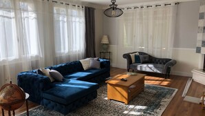 A living room with a blue sofa, a wooden coffee table, a globe, and a patterned rug. - Gite La Garonne with Shared Pool, Communal Garden, and Wi-Fi (Le Lédat)