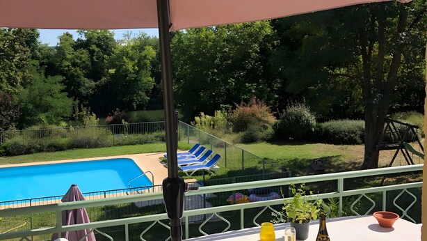 A patio table with a table umbrella, a pool, and lounge chairs in the background. - Gite La Garonne with Shared Pool, Communal Garden, and Wi-Fi (Le Lédat)