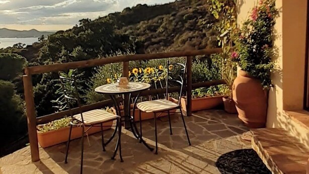 A terrace with a table and chairs, overlooking a scenic landscape with hills and a body of water. - Nature Refuge with Sea Views and Dream Sunsets on Elba Island (Toscana)