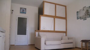 A living room with a beige sofa, a wooden coffee table, and a small wooden stool. There is a door with a glass panel and a framed picture on the wall. - Nature Refuge with Sea Views and Dream Sunsets on Elba Island (Toscana)