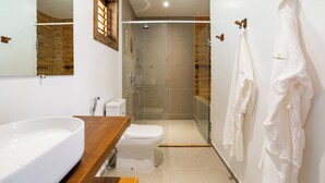A modern bathroom with a wooden vanity, a white sink, a toilet, and a glass-enclosed shower.