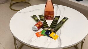 Una mesa redonda con una botella de vino, varias barritas energéticas y una lata de refresco. Un televisor está montado en la pared sobre la mesa.