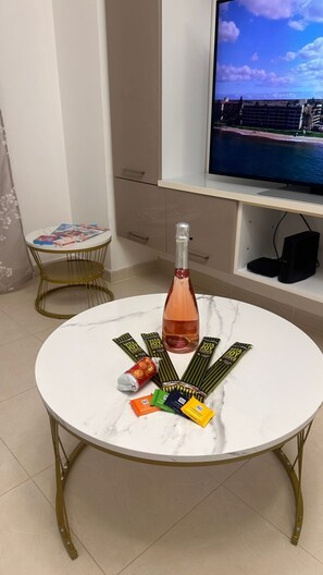 Ein runder Tisch mit einer Weinflasche, mehreren Energieriegeln und einer Limodose. Ein Fernseher ist an der Wand darüber angebracht.
