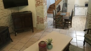 A living room with a TV, wooden cabinet, dining table, chairs, and a staircase leading to another room. - La Maison du Jardin – Country Estate with Large Pool and Wi-Fi (Penne-d'Agenais)