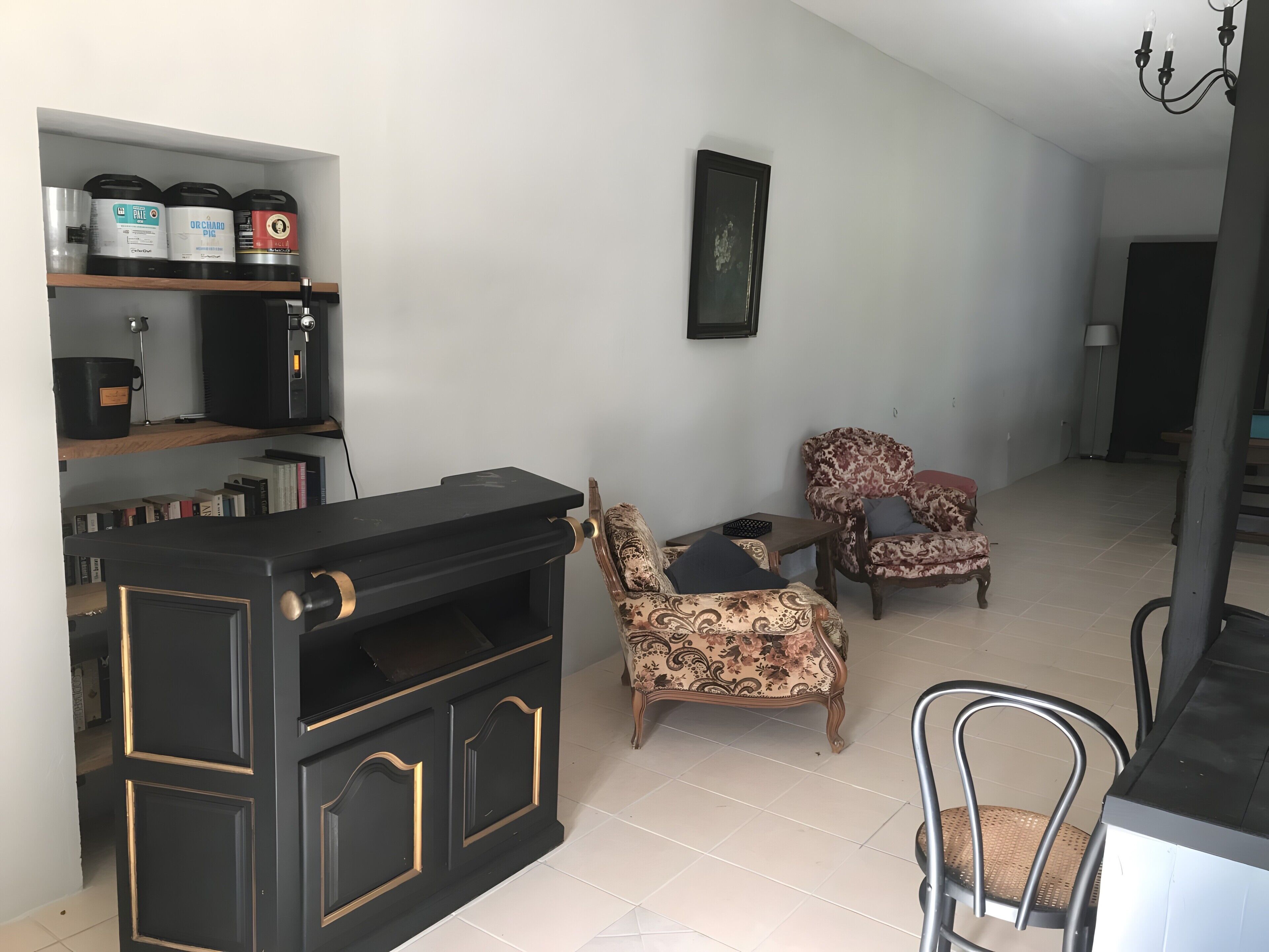 A living room with a black entertainment unit, two patterned armchairs, a bookshelf, and a framed picture on the wall.
