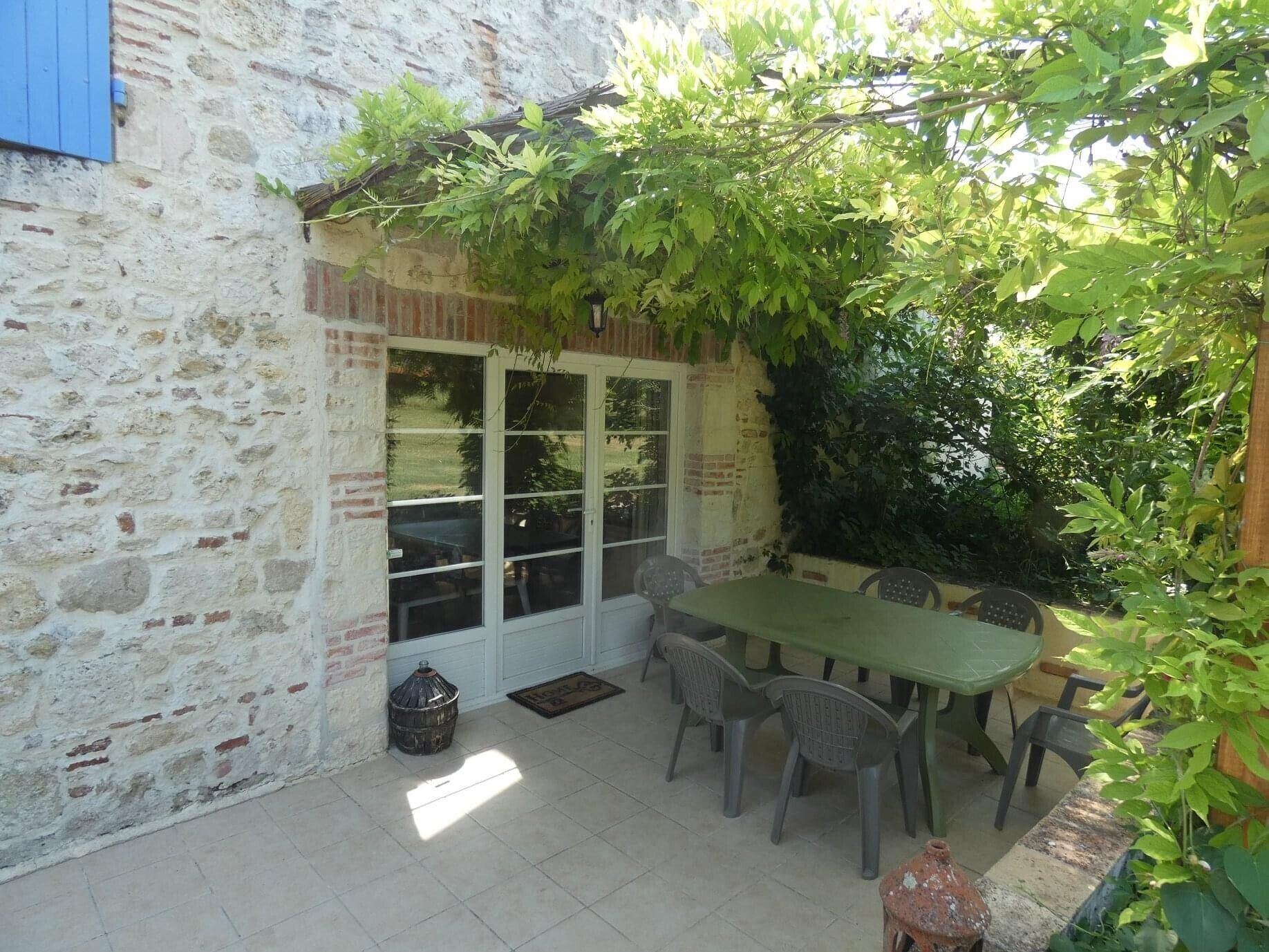 Un bâtiment en pierre doté d’un patio carrelé, d’une table verte et de chaises en plastique.