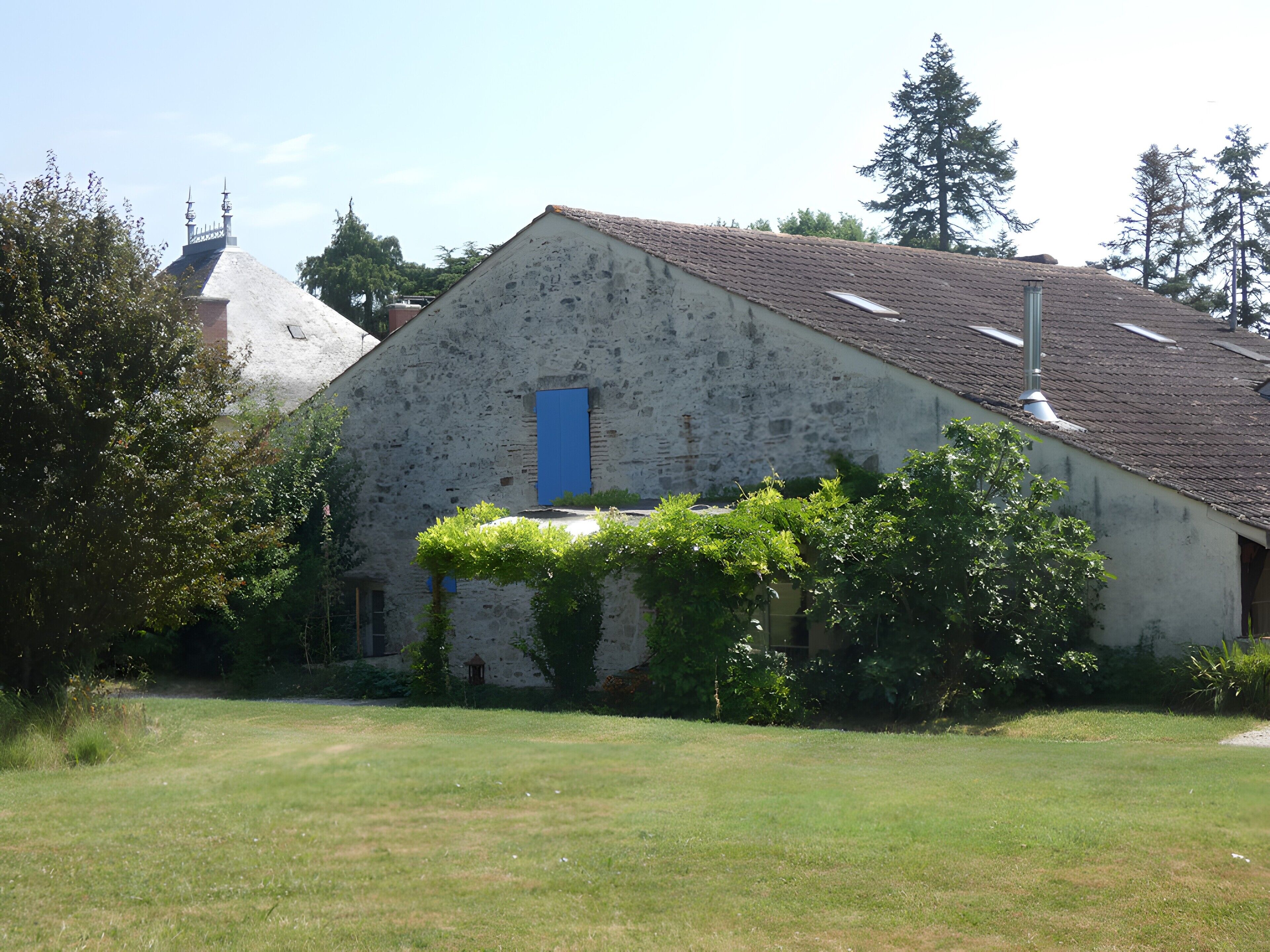 A rustic stone building with a blue door, surrounded by greenery and trees.