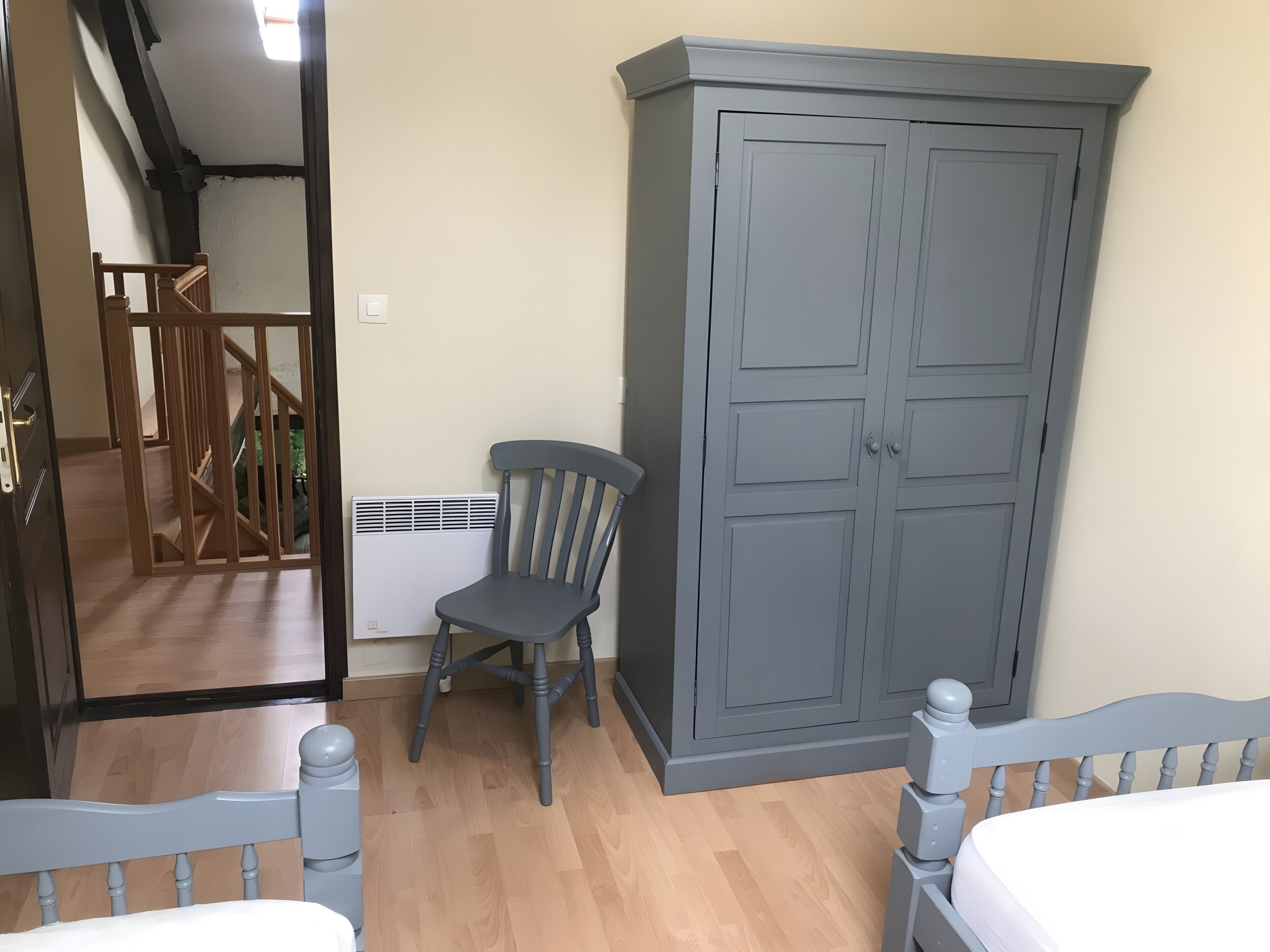 Un dormitorio con una cama de madera, un armario gris y una silla.
