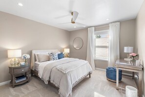Une chambre à coucher comprenant un lit, des tables de chevet, un bureau et un ventilateur de plafond.