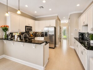 A modern kitchen with white cabinets, a central island, stainless steel appliances, and pendant lighting. - Reunion Resort Villa + Water Park Access + Heated Pool & Spa + Disney Shuttle (Reunion)