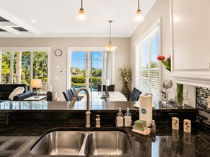 A modern kitchen with a large island, stainless steel sinks, and a dining area with a view of a pool. - Reunion Resort Villa + Water Park Access + Heated Pool & Spa + Disney Shuttle (Reunion)