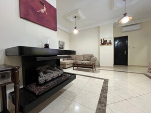 A living room with a fireplace, a sofa, a coffee table, and a door. - Central Secured Compound 2-bedroom apartment in Amman with AC and comfort (Amman)
