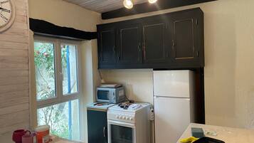 A compact kitchen with a stove, microwave, and refrigerator, a window with a view, and a clock on the wall.