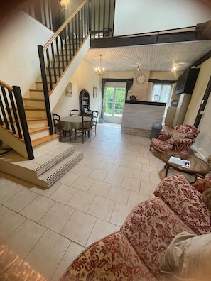 Un vaste espace de vie comprenant un escalier, une table à manger avec des chaises, un coin cuisine et des canapés à motifs.