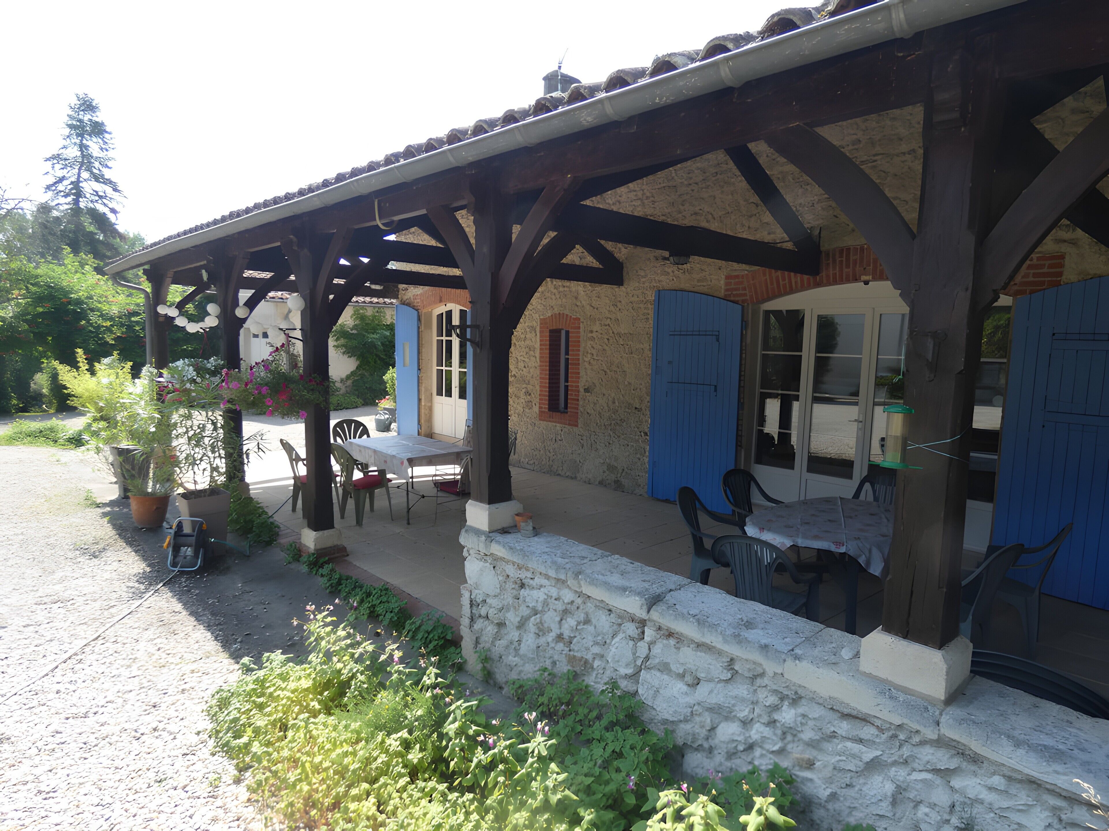 A covered outdoor seating area with a table and chairs, a stone wall, and a blue door.