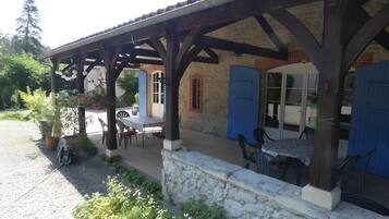 A covered outdoor seating area with a table and chairs, a stone wall, and a blue door.