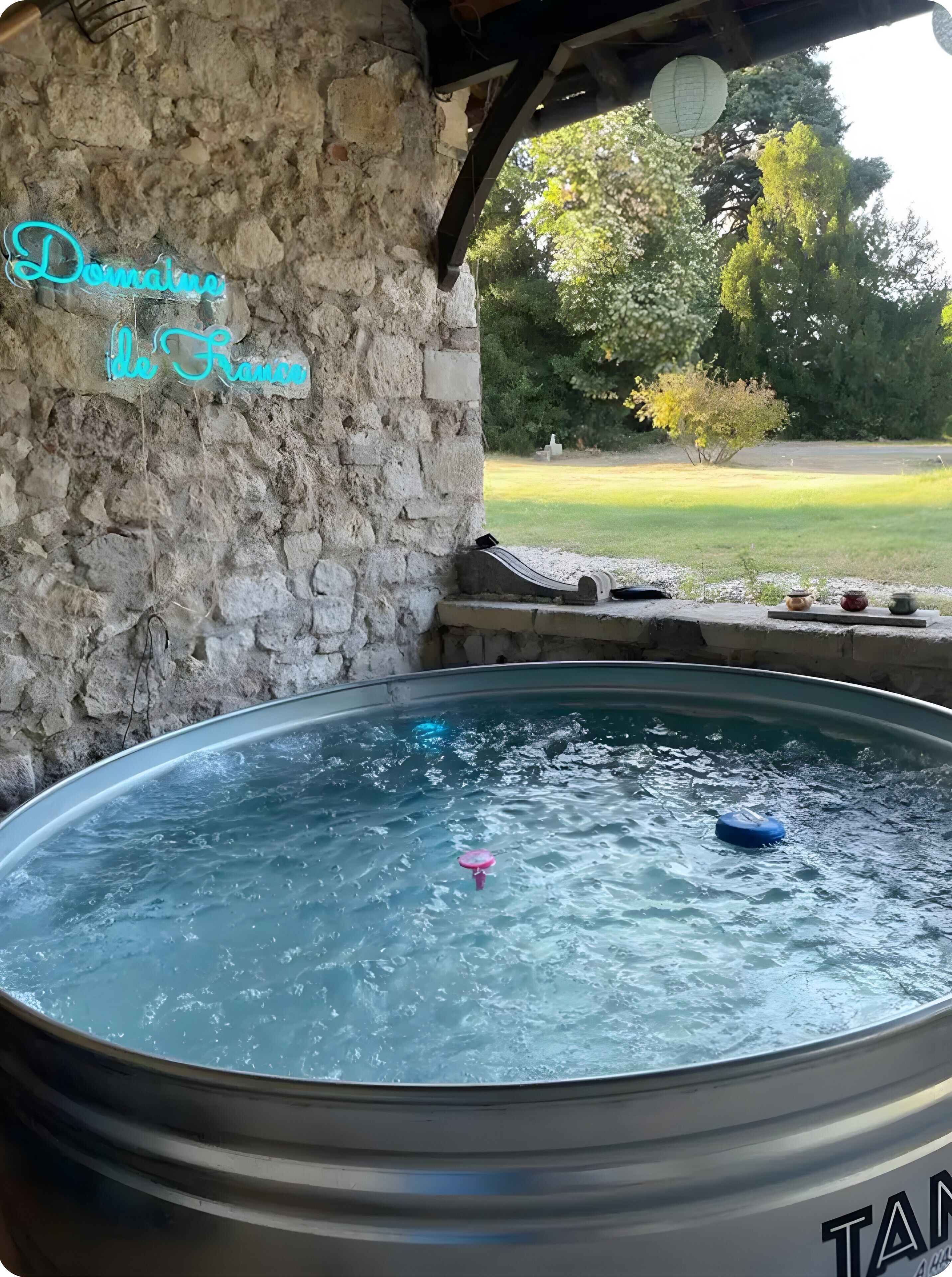 A hot tub with a stone wall and a view of a grassy area.