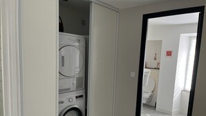 Een wasruimte met een Bosch wasmachine en droger, een spiegel, en een toilet zichtbaar in de aangrenzende badkamer.