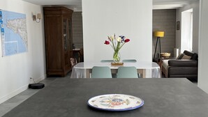 Een eetgedeelte met een tafel, stoelen, een vaas met bloemen, een kaart aan de muur en een kast.