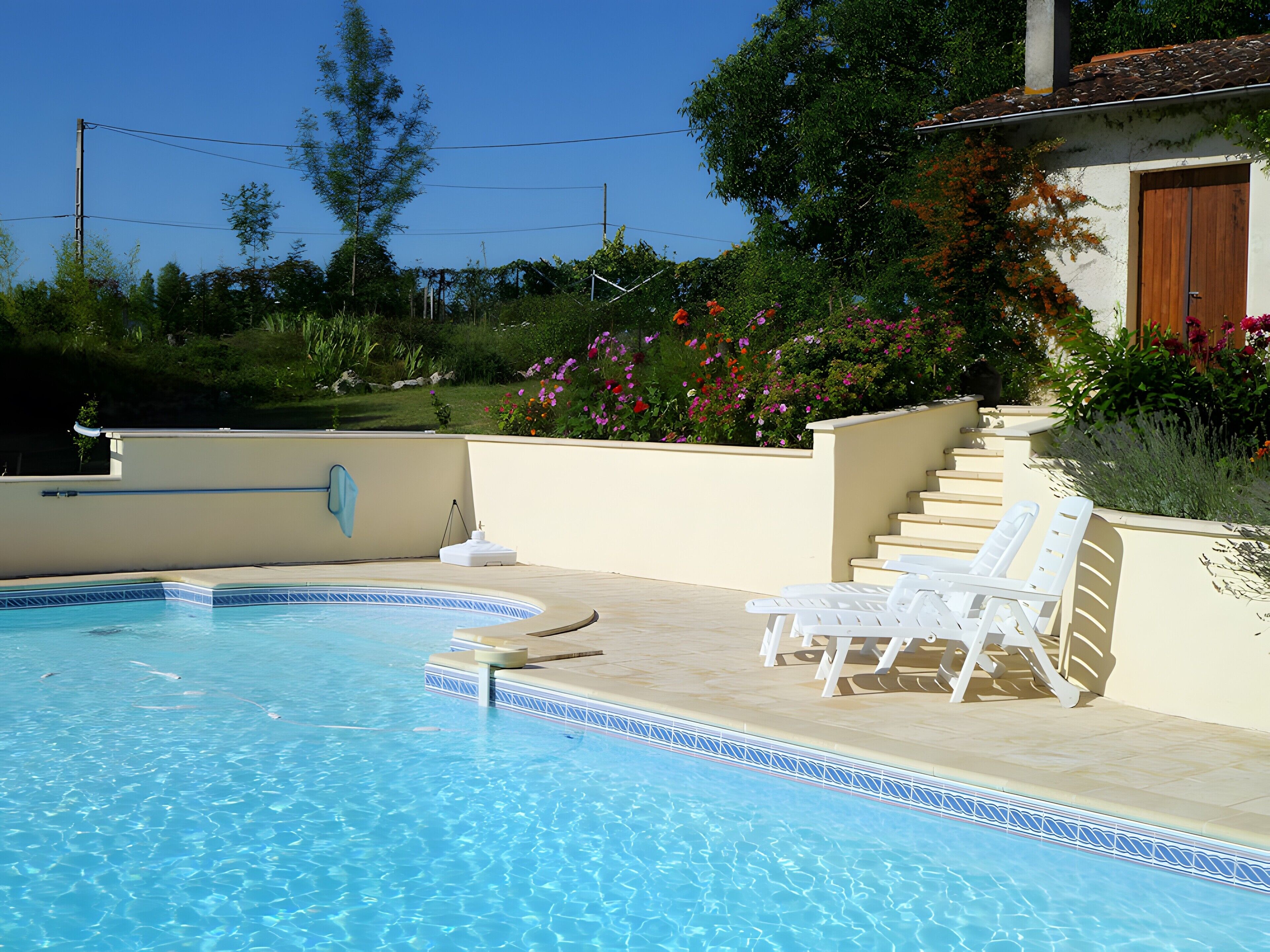A swimming pool with clear blue water, surrounded by a beige deck and white lounge chairs.