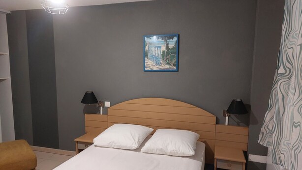 Een hotelkamer met een bed, twee nachtkastjes met lampen, een stoel en een schilderij aan de muur.