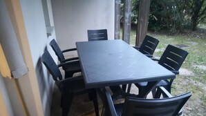 Een rechthoekige buitentafel met zes stoelen, geplaatst tegen een muur met uitzicht op een tuin.