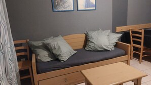 Een kleine kamer met een houten bed, twee kussens, een houten tafel en twee foto's in lijsten aan de muur.