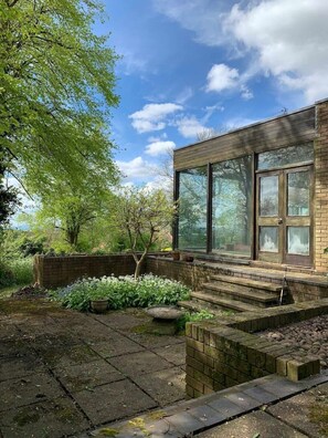 A modern house with large windows, a brick exterior, and a garden with stepping stones and plants. - Mid-Century Masterpiece (Dudley)