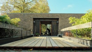 Een modern terras buiten met een houten vloer, een bakstenen muur en een grote deur.