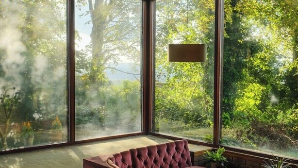 Een moderne woonkamer met een groot raam, een hoekbank en een hanglamp.