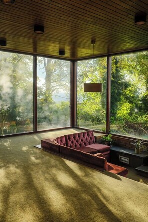 Ein modernes Wohnzimmer mit großem Fenster, einer Eckcouch und einer Pendelleuchte.
