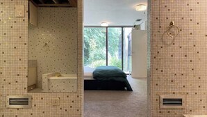 Een moderne badkamer met een grote spiegel, een badkuip en een douchegedeelte. Er is een raam dat natuurlijk licht en uitzicht op groen biedt.