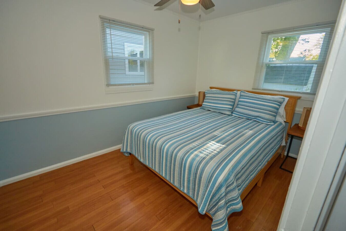 A bedroom with a bed, two windows, a ceiling fan, and wooden flooring.