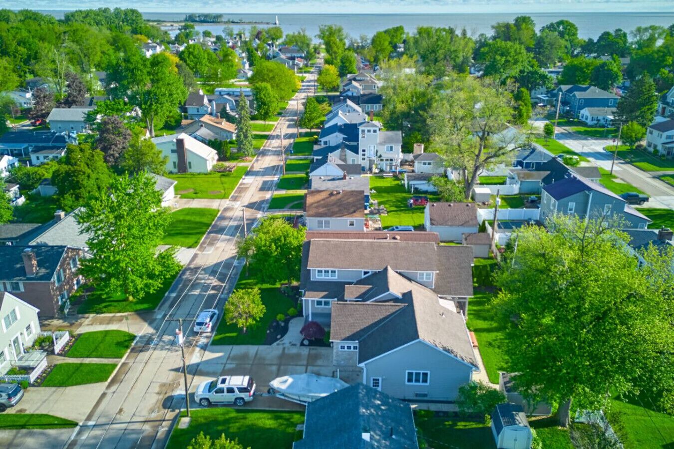 A residential street with houses, a boat, and a clear view of the water.