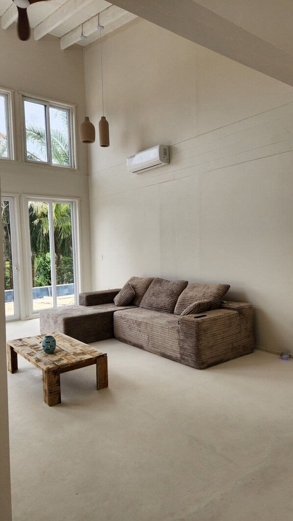 Un salon spacieux doté d’une grande fenêtre, d’un canapé intégré, d’une table basse en bois et d’un ventilateur de plafond.