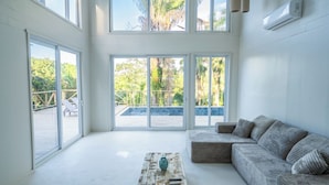 A spacious room with large windows, a sofa, a wooden coffee table, and an air conditioning unit.