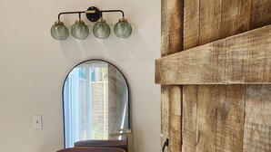 A room with a wooden door, a white shelf with a bowl, and a wall-mounted mirror with three lights.
