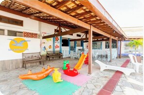 Ein überdachter Außenbereich mit Kinderspielplatz, einschließlich Rutschen und Spielgeräten, sowie eine Wand mit Logo und Kunstwerk.