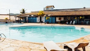 A swimming pool with lounge chairs, a building with a tiled roof, and a clear sky. - A retreat with a garden and swimming pool next to the lagoon. (Iguaba Grande)