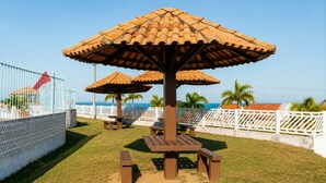 A beachside patio with a wooden table and benches, surrounded by white fences and palm trees. - A retreat with a garden and swimming pool next to the lagoon. (Iguaba Grande)