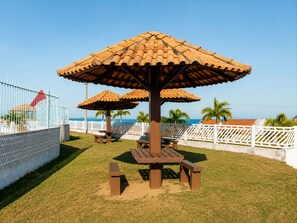 Eine Terrassensitzgruppe am Strand mit einem Holztisch und Bänken, umgeben von weißen Zäunen und Palmen.
