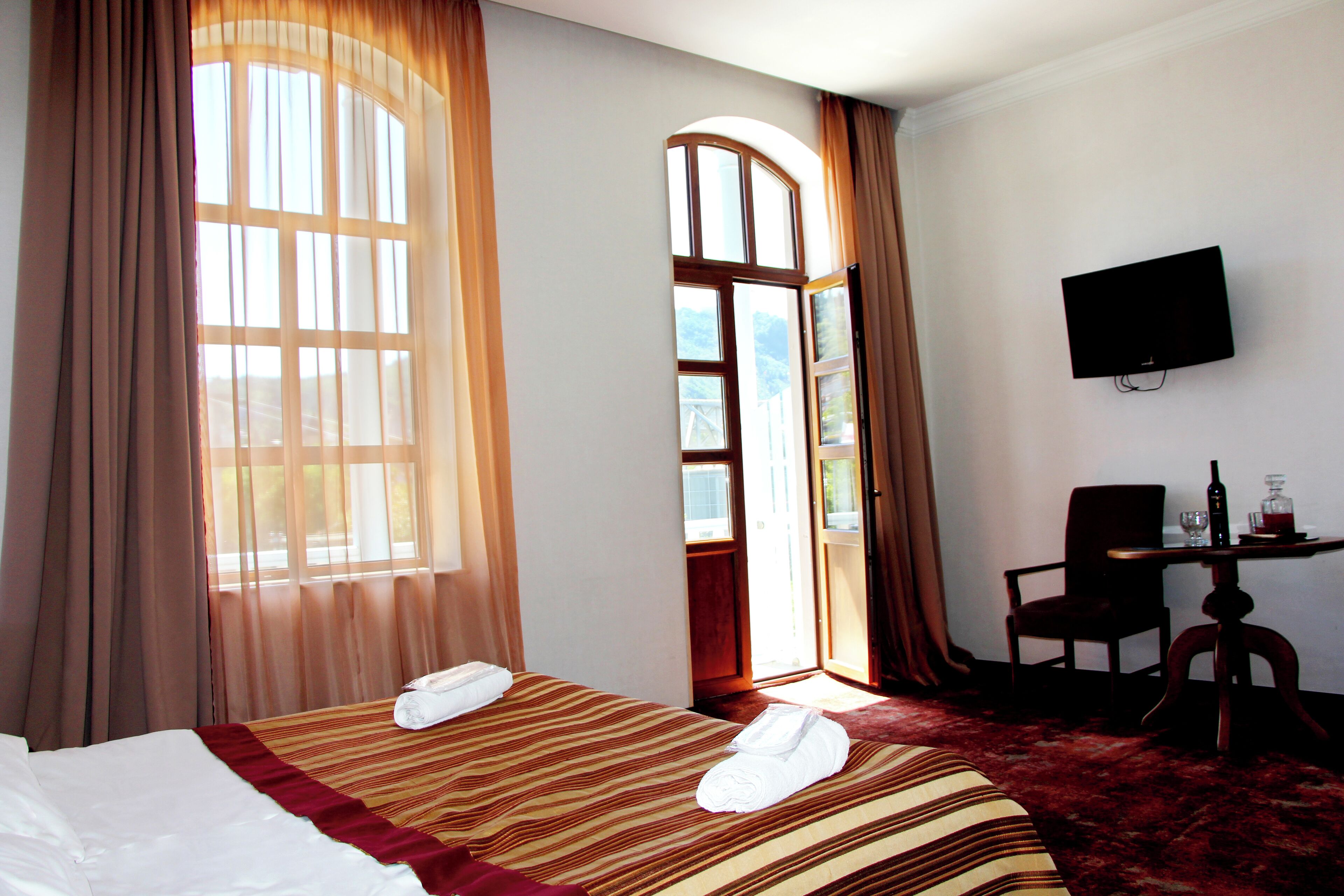 Ein Hotelzimmer mit zwei Betten, einem Fernseher, einem Schreibtisch mit Stuhl und einem großen Fenster mit Vorhängen.
