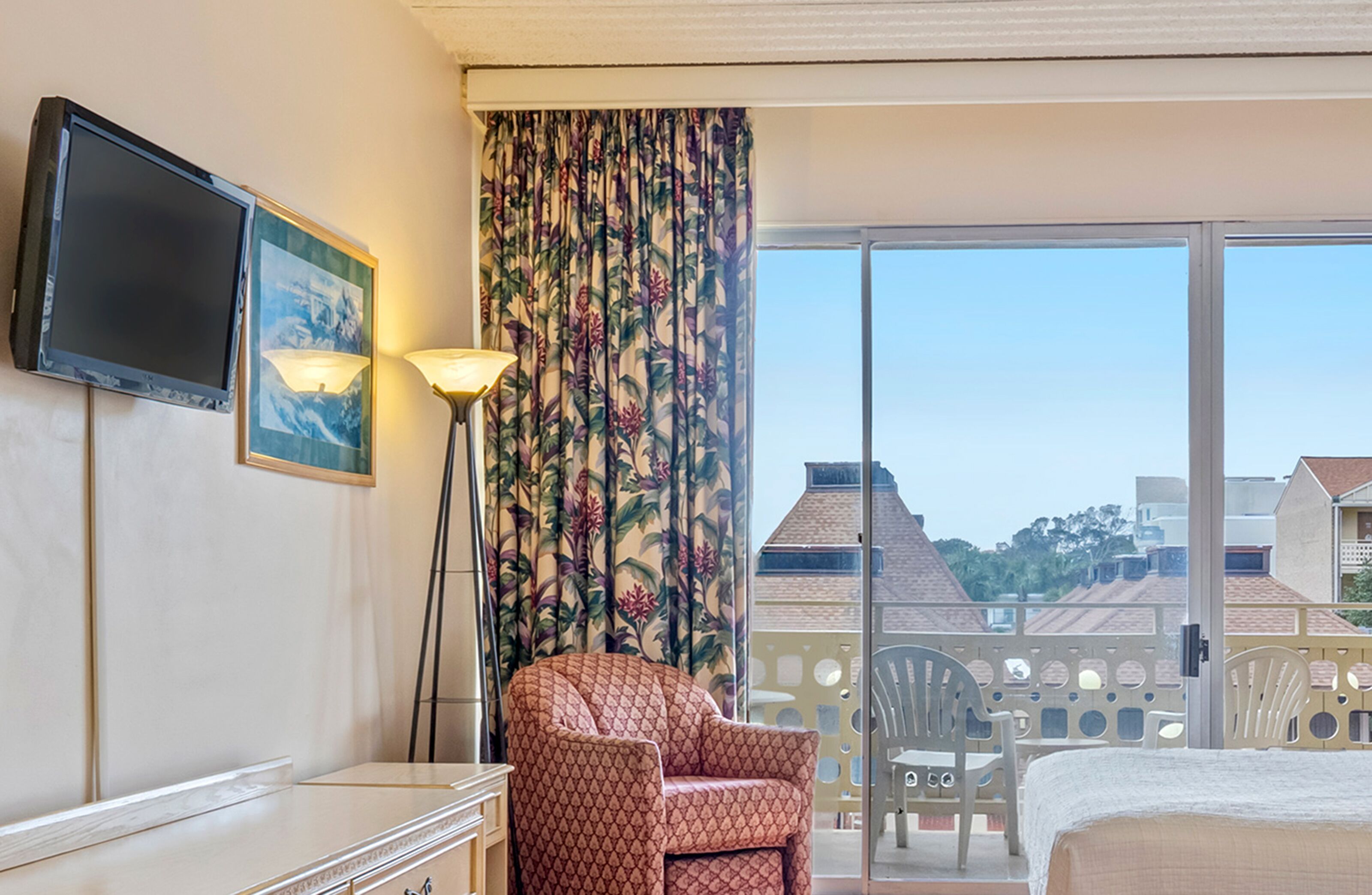 A hotel room with a bed, a chair, a TV, and a window with a view of buildings.