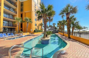 A hotel pool area with a clear blue pool, sun loungers, palm trees, and a yellow building facade. - St. John's Inn (Myrtle Beach)